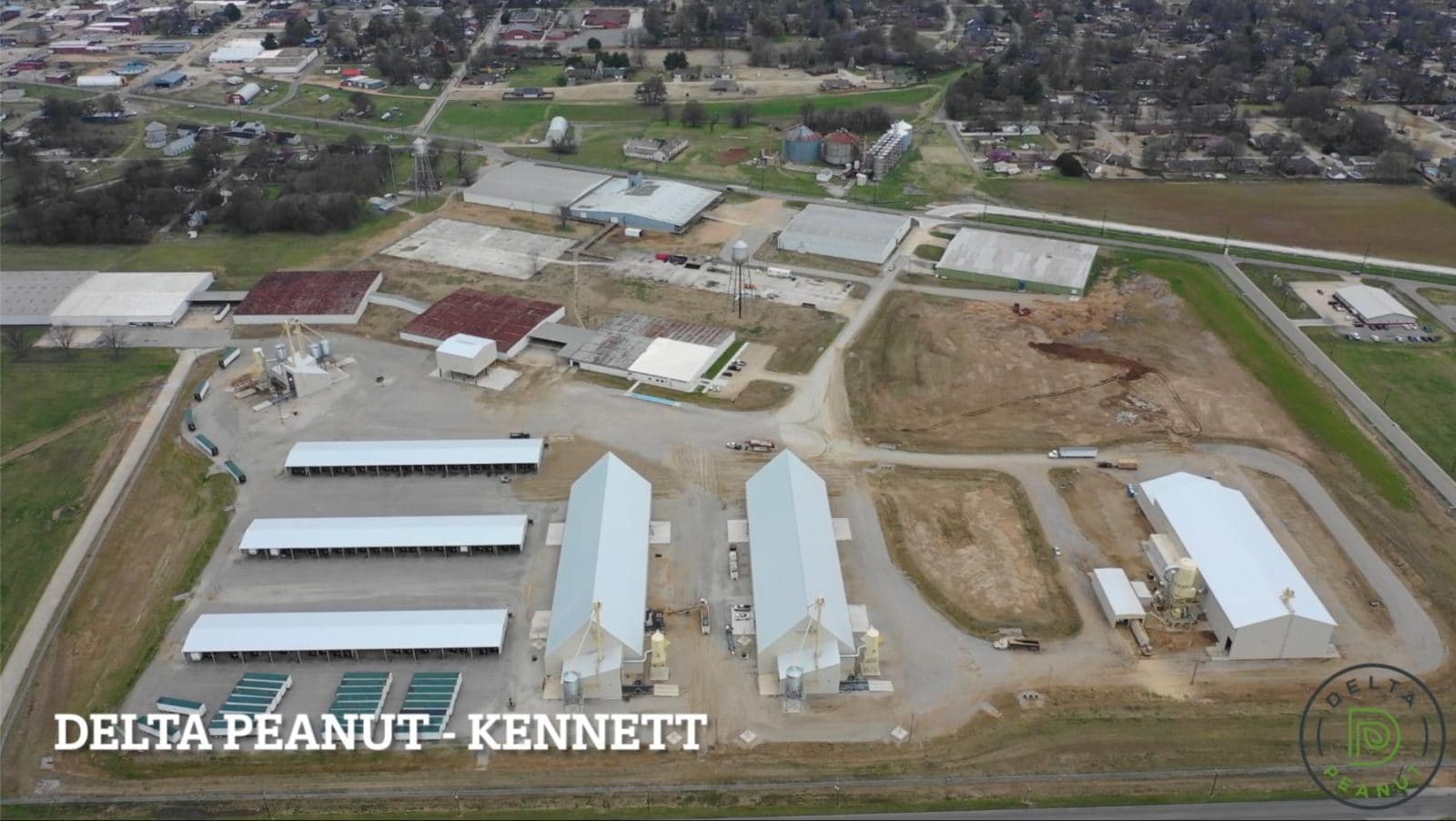 Aerial view of the Delta Peanut processing facility in Kennett, showing multiple warehouse buildings, open lots, and surrounding roads.